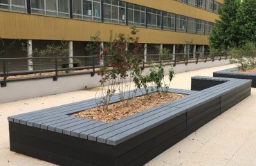 Jardinière urbaine devant bâtiment jaune.