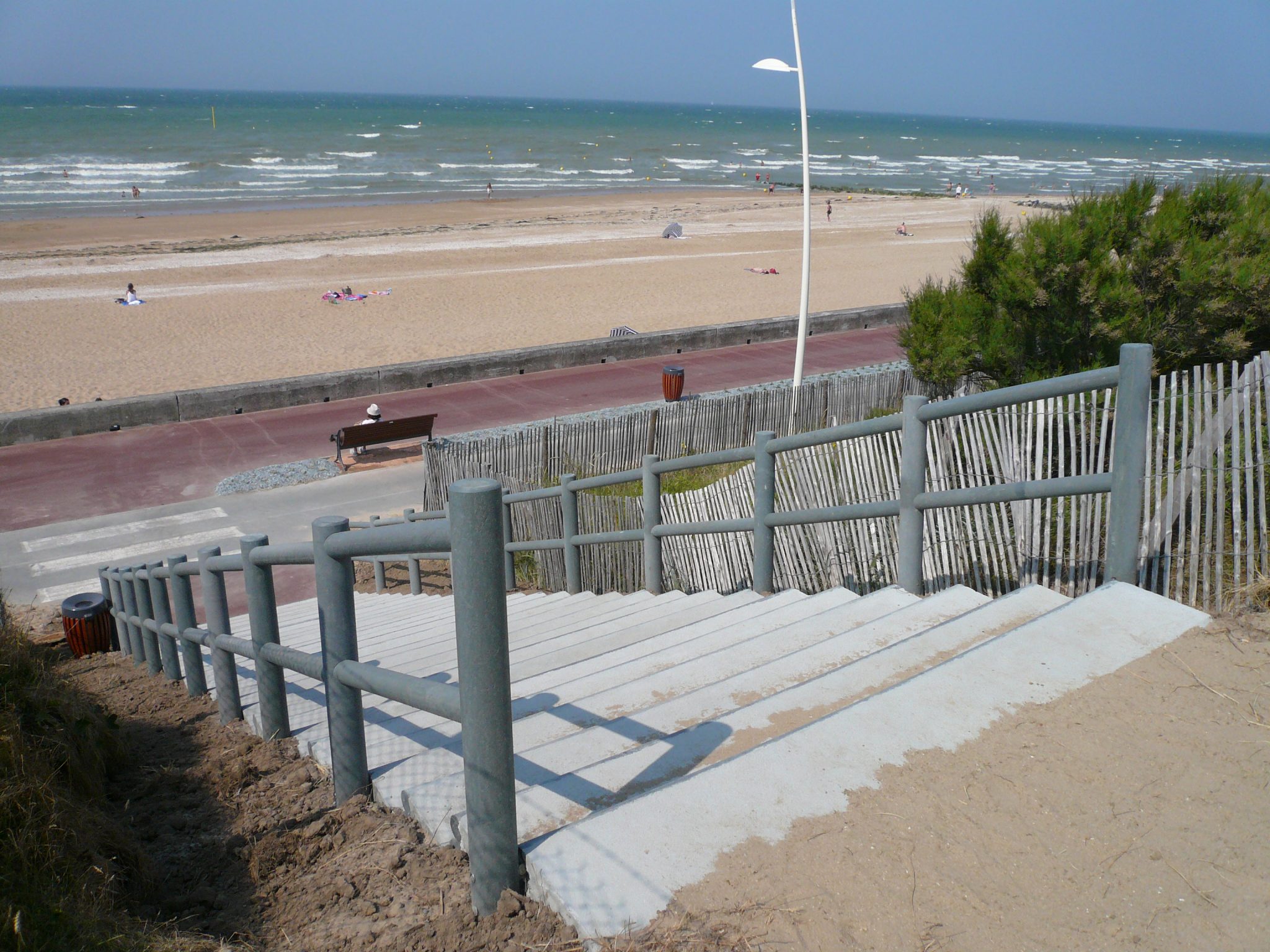 Accès plage avec escalier, dunes et mer.